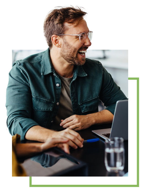 Man in glasses smiling and sitting in front of a laptop.