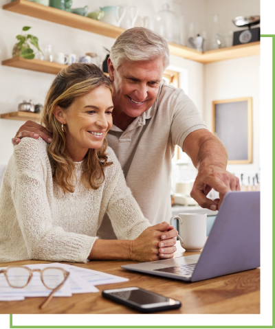 A man and a woman smile while looking at a laptop in a kitchen