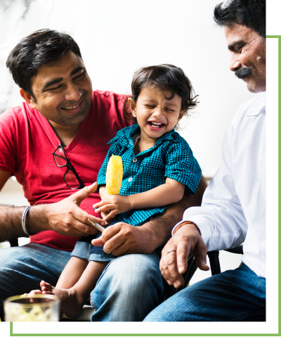 A child laughs while holding onto a yellow disc, two men sit on either side of the child smiling